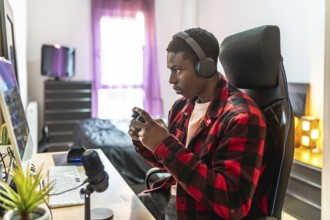 Young man concentrating on playing video games, using headphones and a controller, in his bedroom
