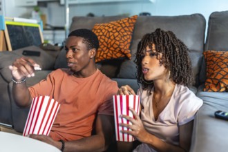 Relaxed couple enjoying a movie night at home, sitting on the floor in front of their sofa and