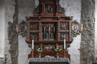 Richly decorated wooden altar in front of a stone wall, adorned with images of saints, candles and