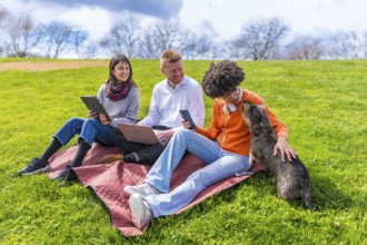 Three young coworkers are taking a break from work outdoors, using laptop, tablet and smartphone,