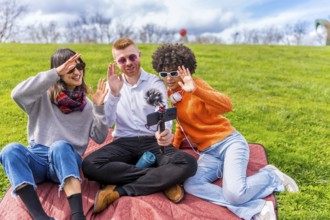 Three content creators waving cheerfully at the camera while filming a video blog outdoors in a