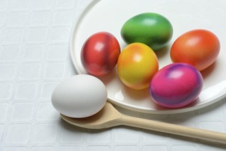 Coloured eggs on a plate and uncoloured eggs on a spoon, Easter celebration