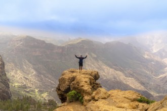 Hiker celebrating at the summit of roque nublo in gran canaria, soaking in stunning views of the
