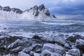 Iced rocks on the beach of Stokkness, behind them the snowy rocky slopes of Vestrahorn, near Höfn,