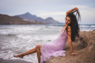 Portrait of a young brunette Caucasian woman in a pink cloth dress, on the beach by the sea in Cabo