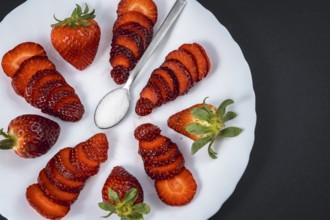 Natural strawberries on a white plate with a spoon of sugar with black background