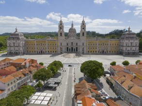 Historic baroque-style palace with yellow façade and two towers, under blue sky and large square,
