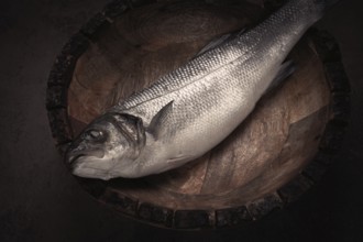 Fresh, raw sea bass fish, in a wooden plate, top view, no people
