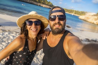 A man and woman are posing for a picture on a beach. The man is wearing a black tank top and