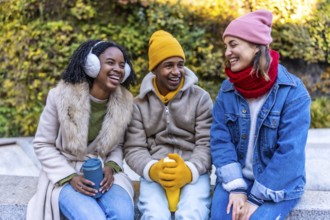 Three cheerful young multi ethnic friends sitting outdoors in the city on a cold winter day,