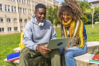 Smiling young multiethnic students studying together with a laptop sitting on campus