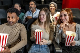 Happy multi ethnic friends watching film together and eating popcorn, having fun at the movie