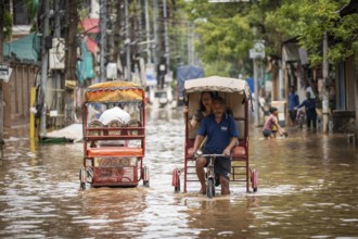 Commuters in cycle rickshaws as they wade through a flooded street after heavy rains in Guwahati,