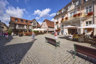Market square with benches, historic buildings and half-timbered houses under a blue sky with