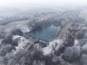 Aerial view of a small lake surrounded by winter hoar frost in a peaceful landscape, Gechingen,