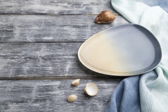 Empty blue ceramic plate on gray wooden background and blue textile. Side view, copy space