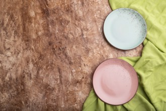 Two empty blue and pink plates on brown concrete background and green textile. Top view, copy