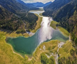 Green mountain landscape with river and lake, sun reflection in the water, surrounded by forests,