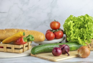 Colourful peppers, tomatoes, cucumber and lettuce next to a baguette on a table, copy room