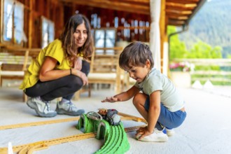 Young boy enjoying a toy train set on a sunny patio with an adult nearby