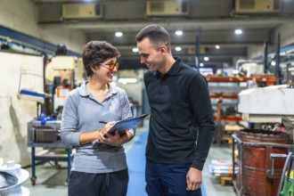 Male worker talking happily to a female workshop manager while writing on clipboard