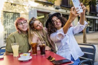 Happy female friends taking selfie sitting on a terrace of a bar