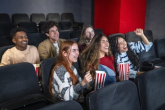 Young people having fun watching a film at the movie theater, eating popcorn and laughing