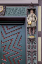Detailed wooden door of a half-timbered house with statue and decorated façade, clear zigzag