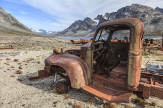 Rusted car and oil drums in front of steep mountains, remains of a US airbase from the Second World