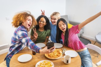 Four diverse friends capture a fun moment with a selfie while having pizza, snacks, and drinks at a