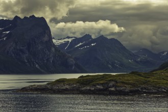 Dramatic mountain silhouette under dark clouds with a calm lake, Norway, Europe