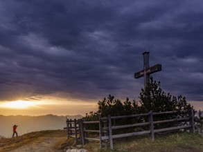 Photographer next to the summit cross on the Roßfeld in a dramatically overcast sky, the sun shines