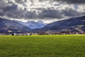Dramatic Alpine landscape with green meadow in the foreground and cloudy sky over a village, Bad