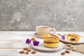 Small cheesecakes with jam and almonds with cup of coffee on a white wooden background and linen