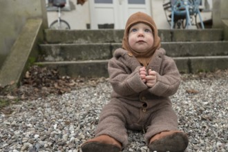 Small child, 8 months, wrapped up warm, sitting on the gravel and playing with stones,