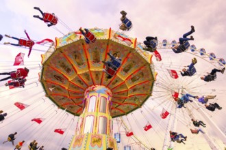 Chain carousel in motion with cheerful people in front of a cloudy sky, Ferris wheel, wave flight,