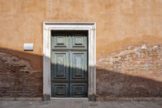 Red house facade with large green door, peeling plaster on brick wall, Venice, Veneto, Italy,