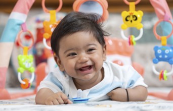 Baby boy playing and smiles lying on bed with pacifier on mouth