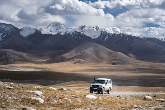 Off-road vehicle on a gravel track, glaciated and snow-covered peaks, Ak Shyrak Mountains, near