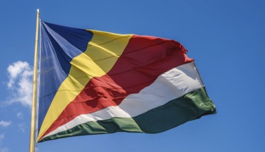 The flag of Seychelles, fluttering in the wind, isolated against a blue sky