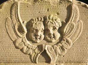 Two angel faces and wings on stone gravestone in church graveyard, Suffolk, England, UK