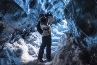 A woman is standing in a cave with snow on the ground. She is wearing a backpack and a white jacket