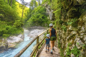 Mother and son wearing helmets walking on wooden path and enjoying breathtaking view of radovna