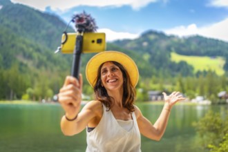 Happy tourist vlogging with smartphone and external microphone at lake dobbiaco, surrounded by the