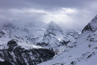 Dark clouds and wafts of mist surround the snow-covered summit of Mount Le Besso, view from the