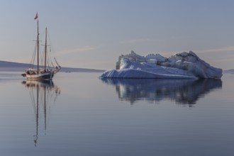 Traditional sailing ship reflected in fjord next to iceberg, sunny, Ittoqqortoormiit, Scoresby