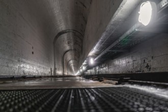 Concrete tunnel with long perspective to the inside, illuminated by lamps at the sides, humid