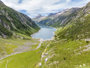 A mountain lake embedded in an alpine landscape with green meadows, mountains, a river and a hiking