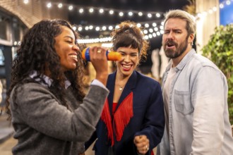 Latin woman singing karaoke next to friends at night party in the terrace of a bar