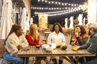Multi-ethnic friends sitting on a bar terrace drinking celebrating together at night